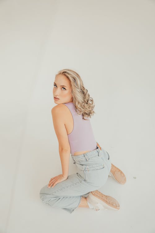 Young Woman in a Tank Top and Jeans Kneeling on the Floor 