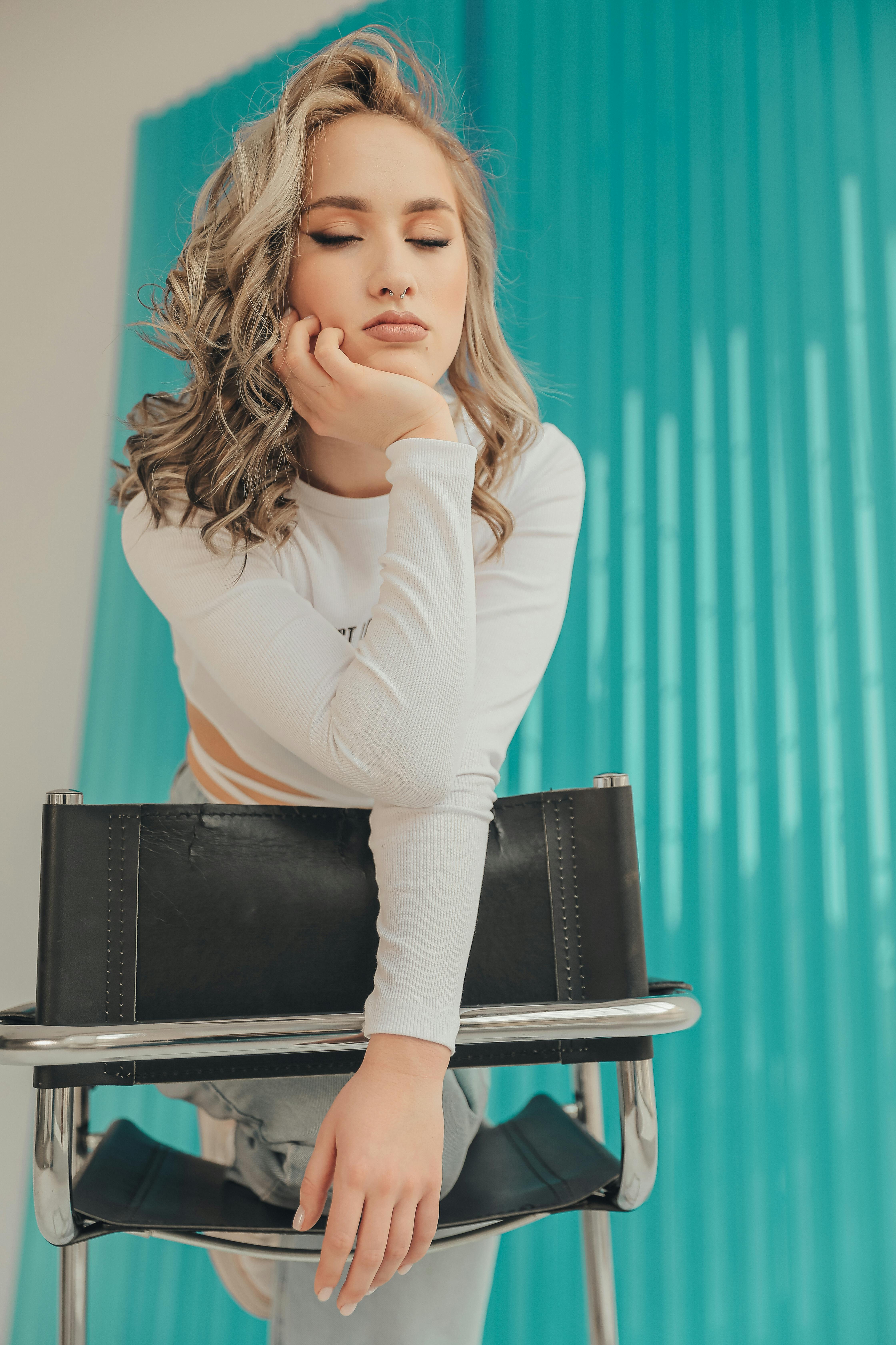 Free Elegant woman in white, posing on a chair in a bright studio with a turquoise backdrop. Stock Photo