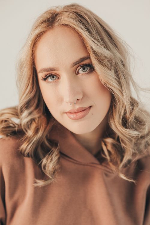 Free Close-up portrait of a young blonde woman with curly hair and a septum piercing against a white background. Stock Photo