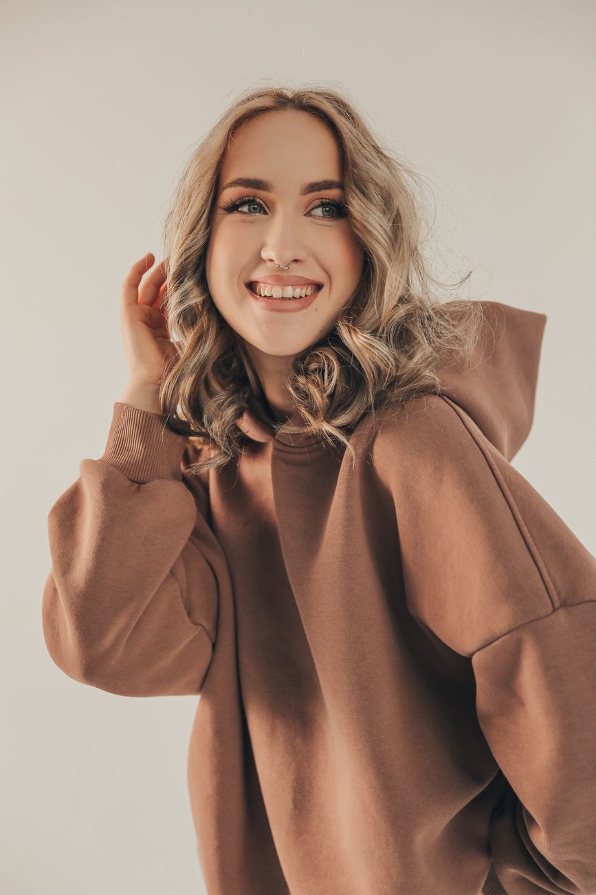 Portrait of a smiling woman in a cozy brown hoodie, posing confidently indoors.