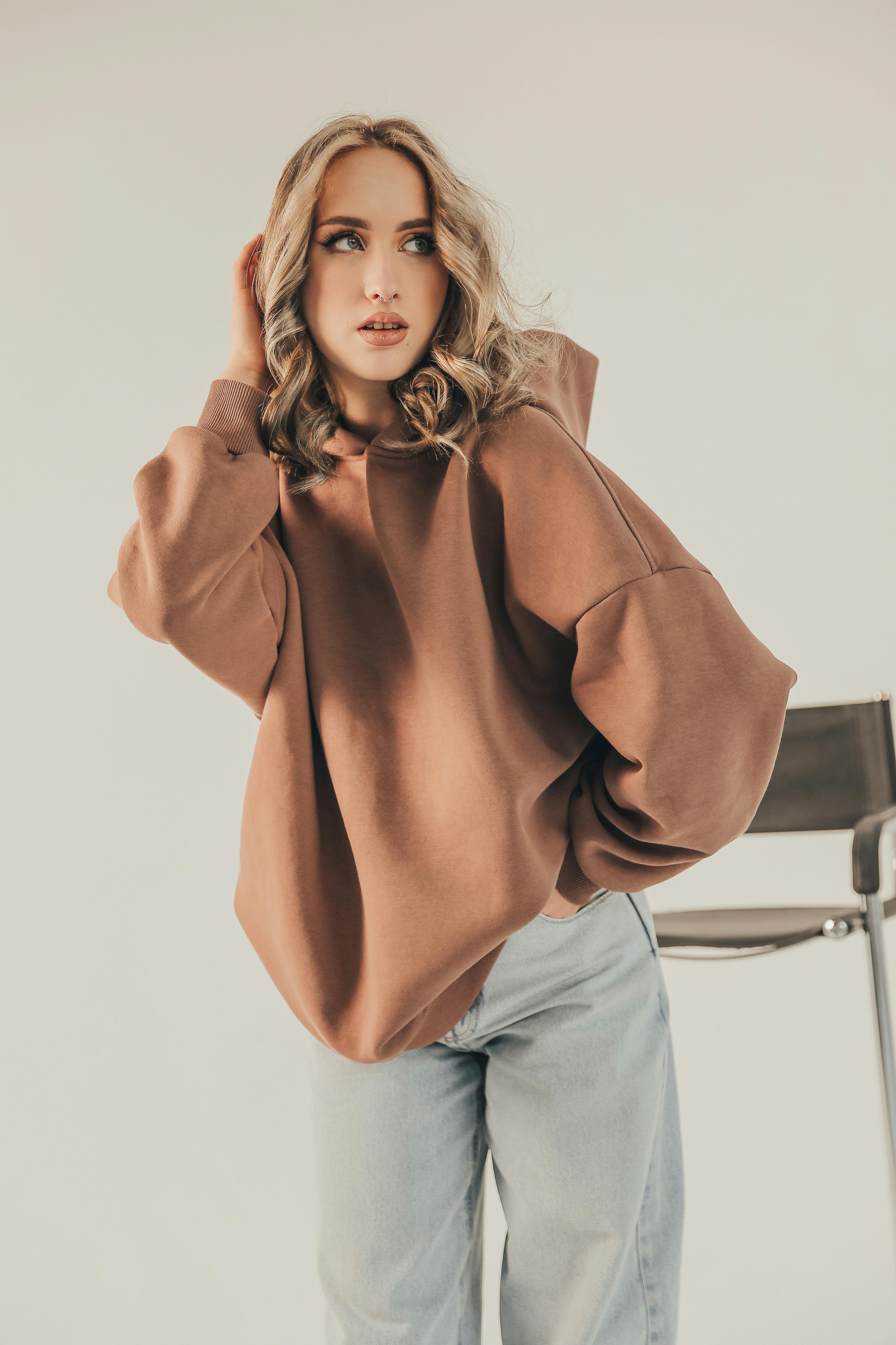 Free Stylish woman in oversized hoodie and jeans posing elegantly indoors. Stock Photo