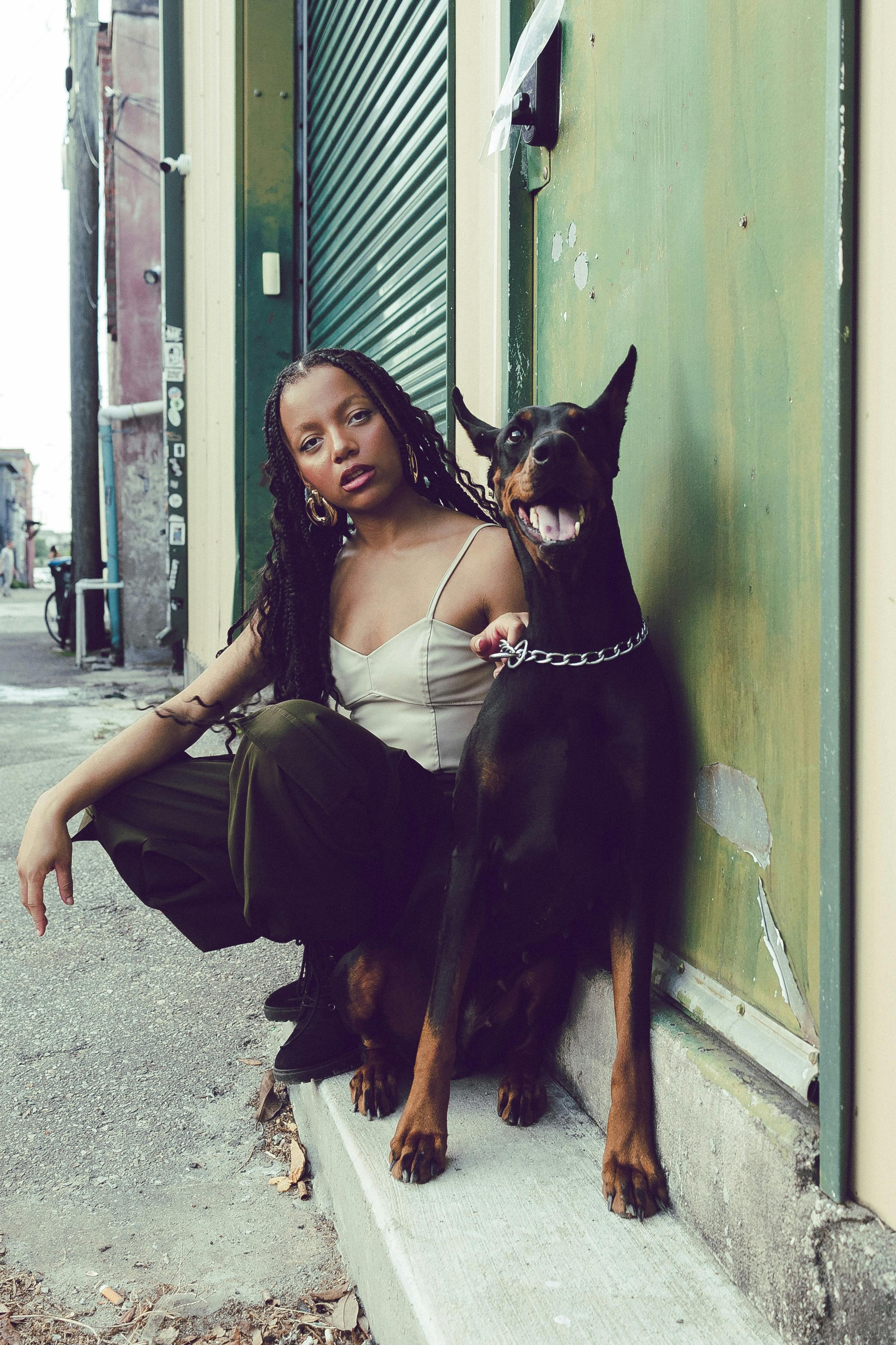 A woman poses with a Doberman on a city street, showcasing urban fashion style.