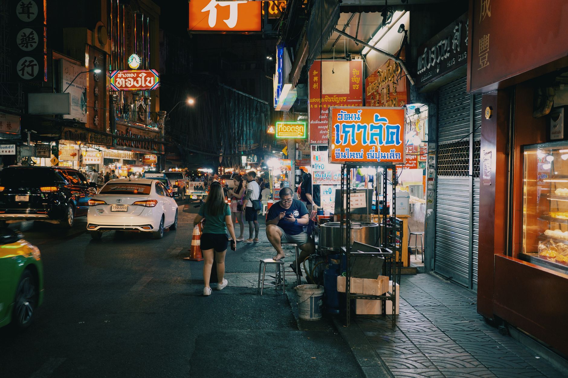 Busy Bangkok street at night with market stalls and motorbikes