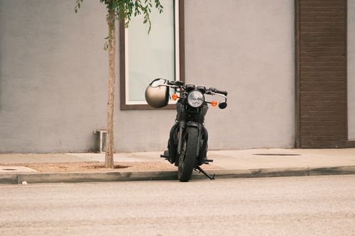 Free A classic motorbike parked against a city building wall on a quiet urban street. Stock Photo