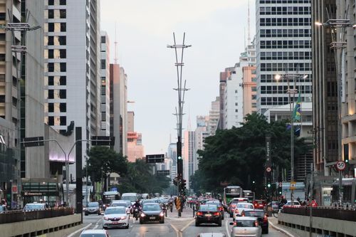Free Lively city street with traffic, tall buildings, and trees, capturing urban energy. Stock Photo