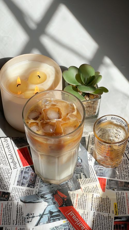 Free A refreshing glass of iced coffee with a wax candle and succulent on a newspaper backdrop. Stock Photo