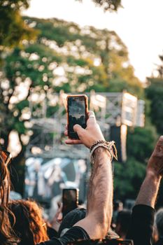 Urban outdoor concert scene with person photographing stage on smartphone in Mendoza, Argentina.