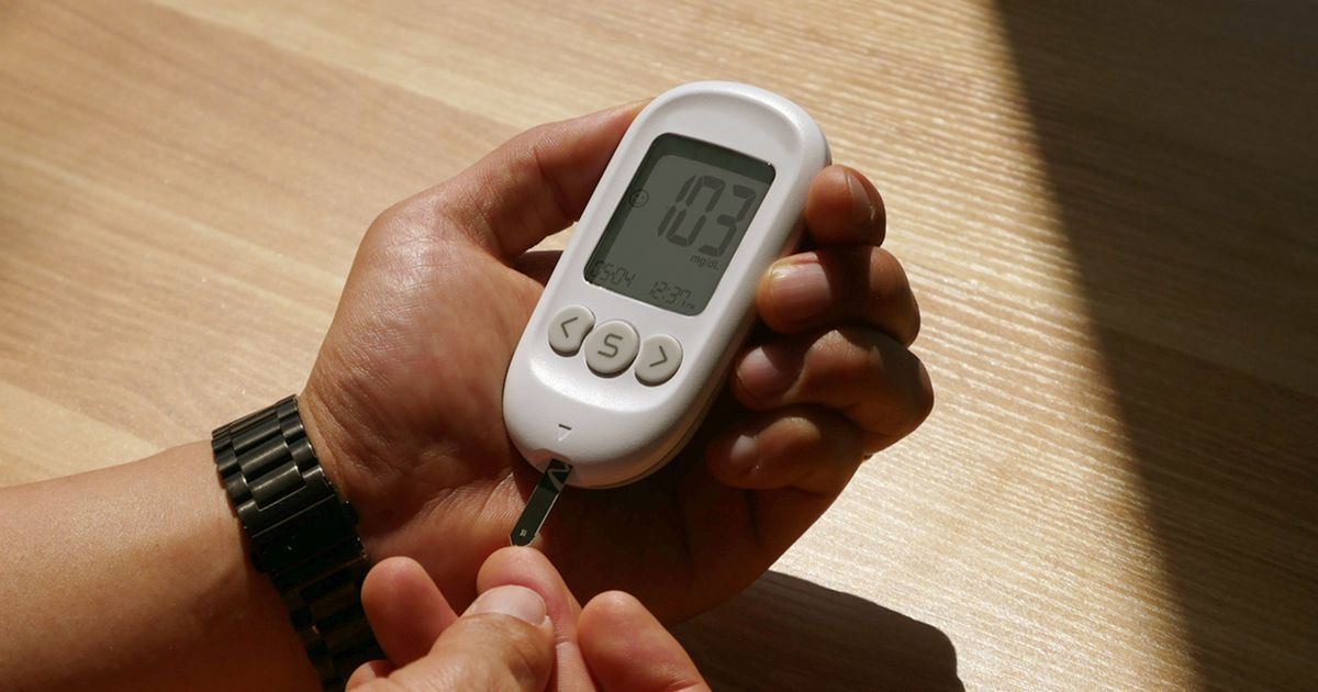 Hands checking blood sugar with a glucose meter at a wooden table