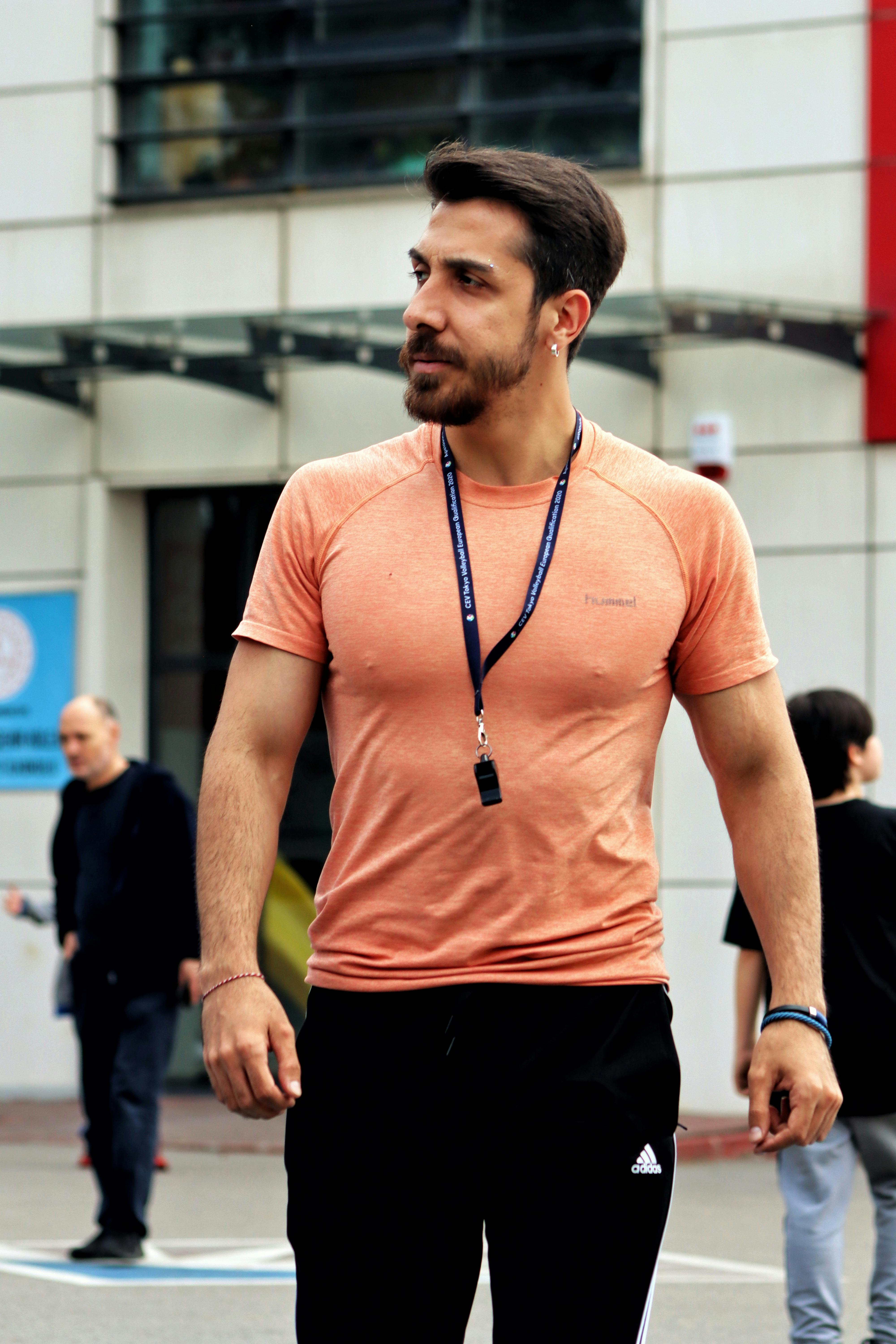 Portrait of a man in an urban setting wearing an orange T-shirt and whistle, epitomizing casual city life.
