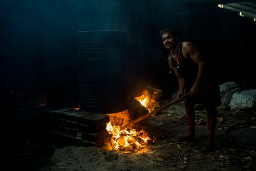 Free A man intensively stokes a fire in a dark setting, reflecting hard work and survival. Stock Photo
