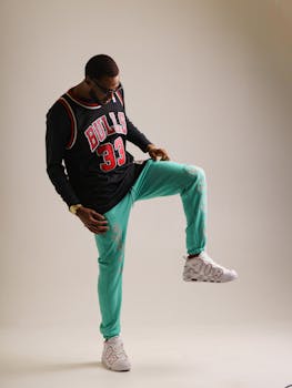Stylish man posing in a basketball jersey and green pants studio shoot.