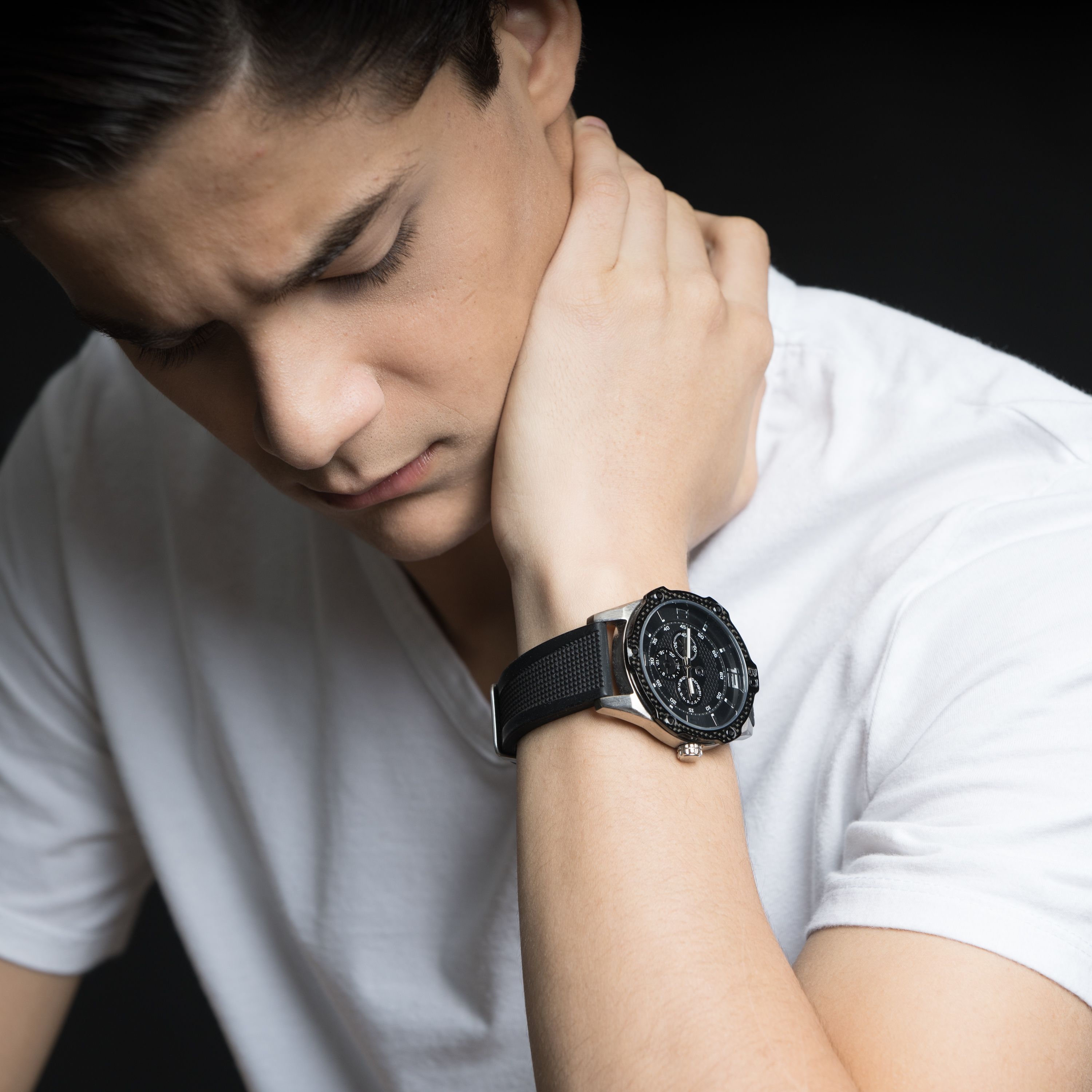 Close-up portrait of a young man in a white t-shirt, looking thoughtful with a wristwatch.