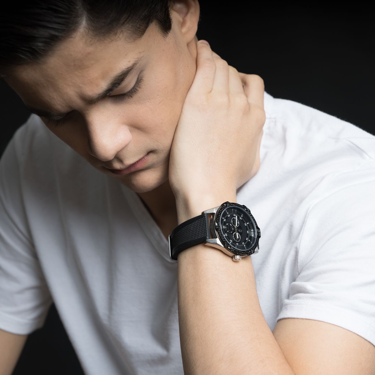 Close-up portrait of a young man in a white t-shirt, looking thoughtful with a wristwatch.