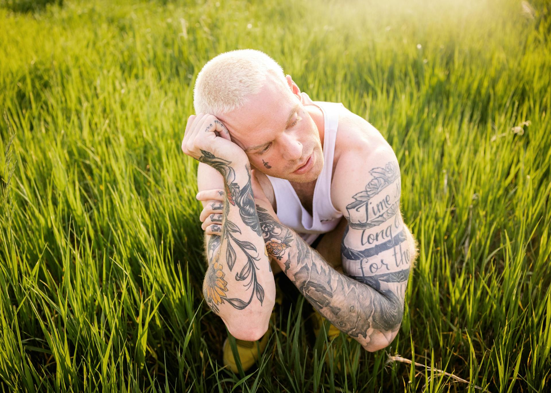 Man with Tattoos and Dyed Hair Squatting on Field