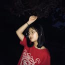 晚上，一名戴着眼镜、穿着红色衬衫的年轻女子在户外摆姿势