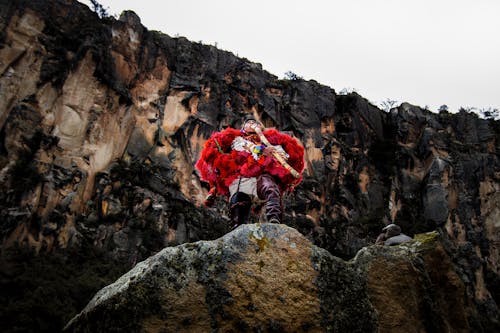 Man in Traditional Clothing Playing Traditional Flute on Rocks