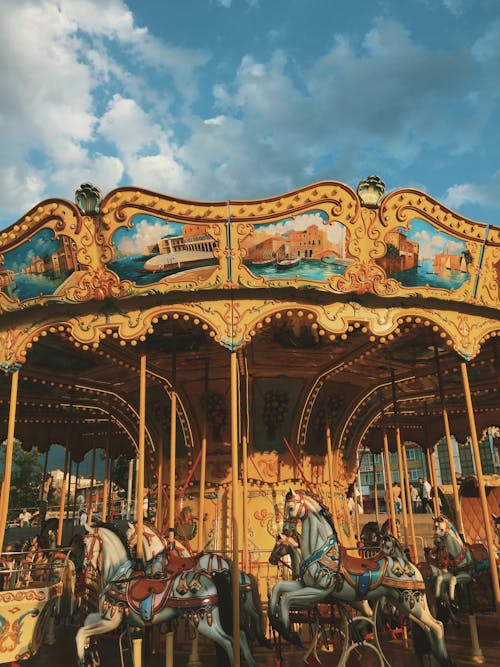 Low angle of round festive carousel horses located in amusement park against cloudy blue sky