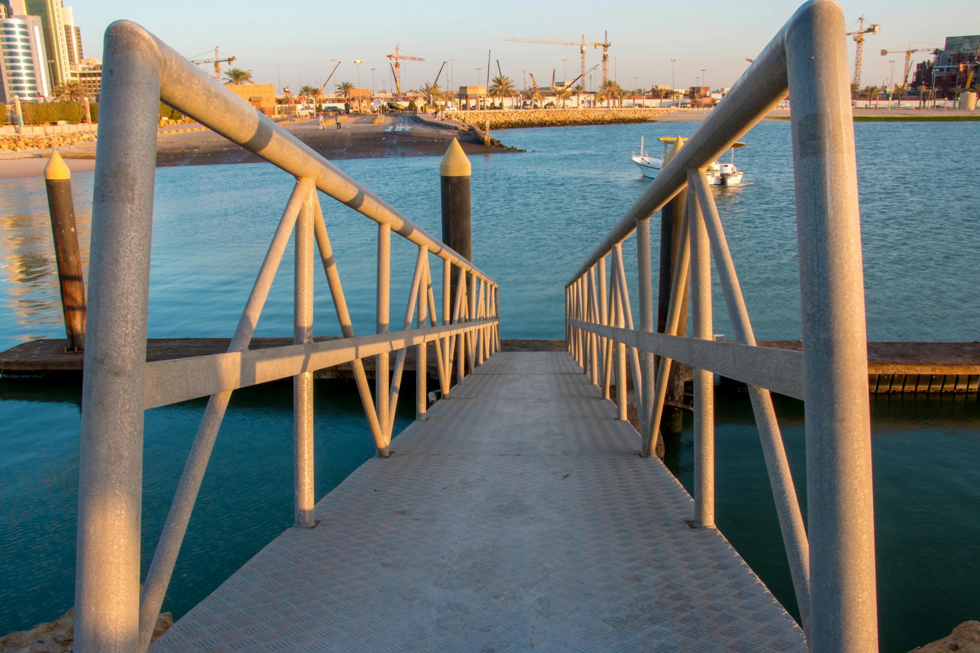 A metal walkway leading to a busy industrial port with cranes and watercraft.