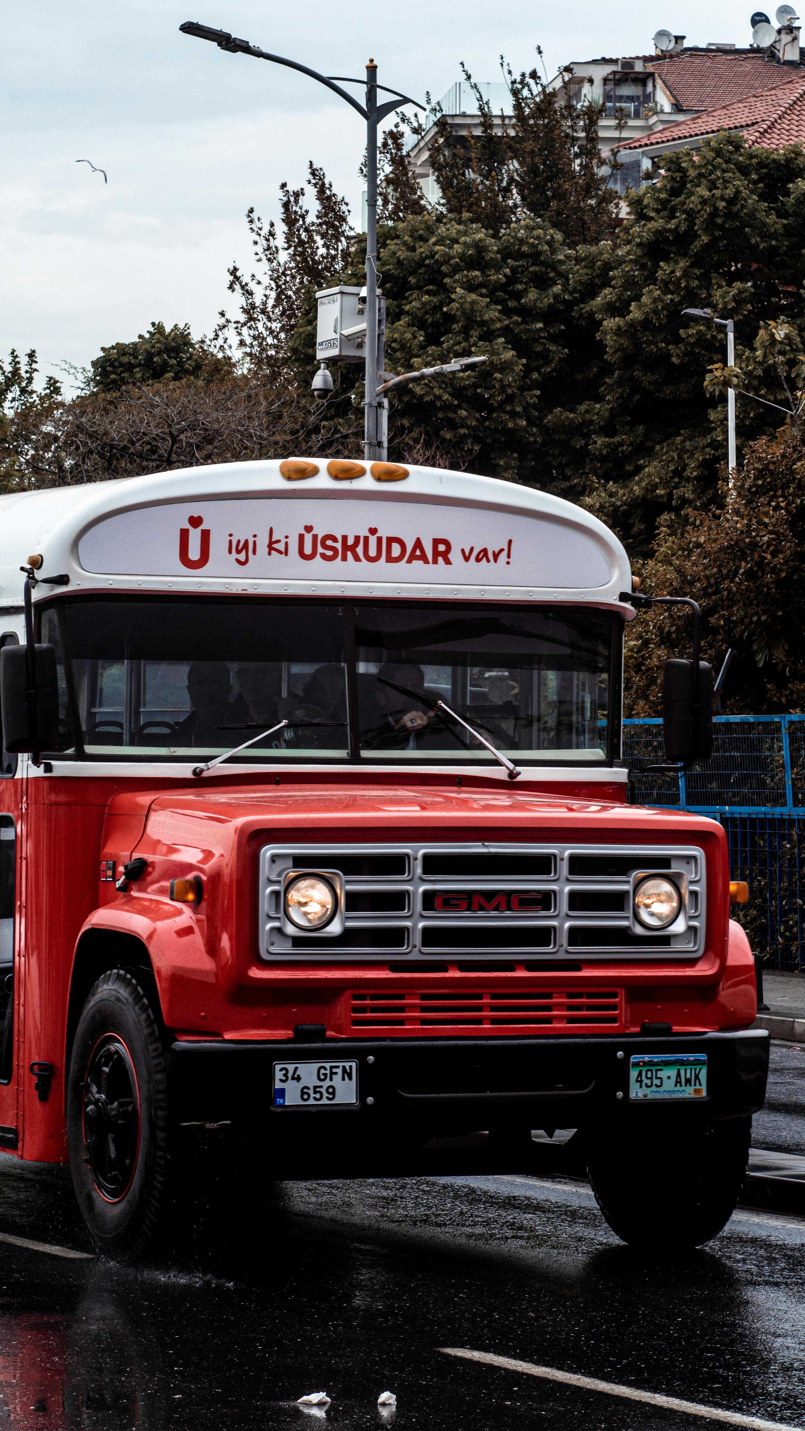 A vintage red bus on a rainy street in Üsküdar, İstanbul, showcasing urban life and transportation.