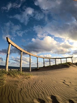 Curved stone arch on sandy beach under dramatic cloudy sky, perfect for travel and nature themes.