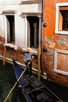 A gondolier in stripes and hat rowing on a Venice canal with colorful building.