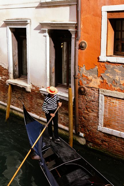 A gondolier in stripes and hat rowing on a Venice canal with colorful building.