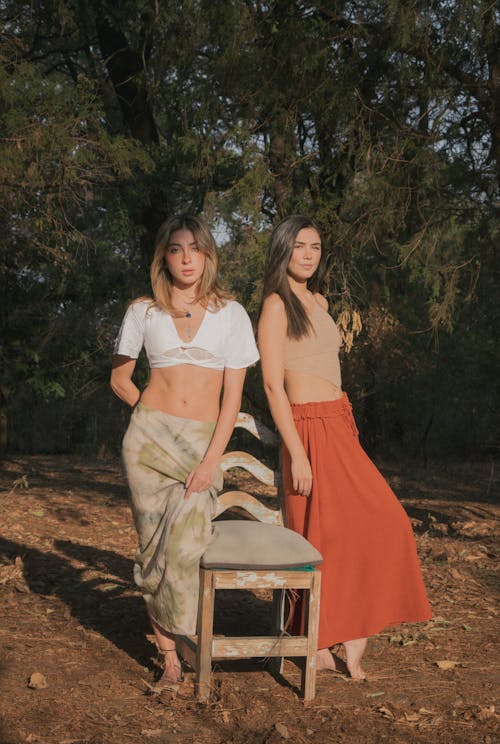 Women Standing Next to a Wooden Chair by the Forest 