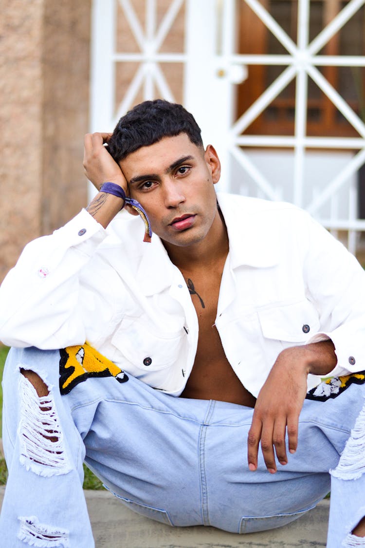 Young Man In A White Jacket And Jeans Sitting On Steps 