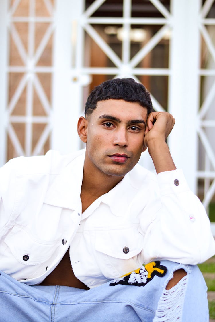 Young Man In A White Jacket And Jeans Sitting On Steps 