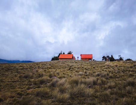 Rural homes with red roofs on a grassy hill under a cloudy sky in Berlin, Santander.