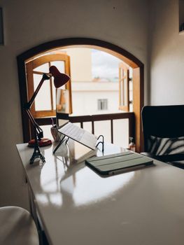 A modern desk setup in a cozy room with a window letting in natural light, featuring a laptop and stylish lamp.