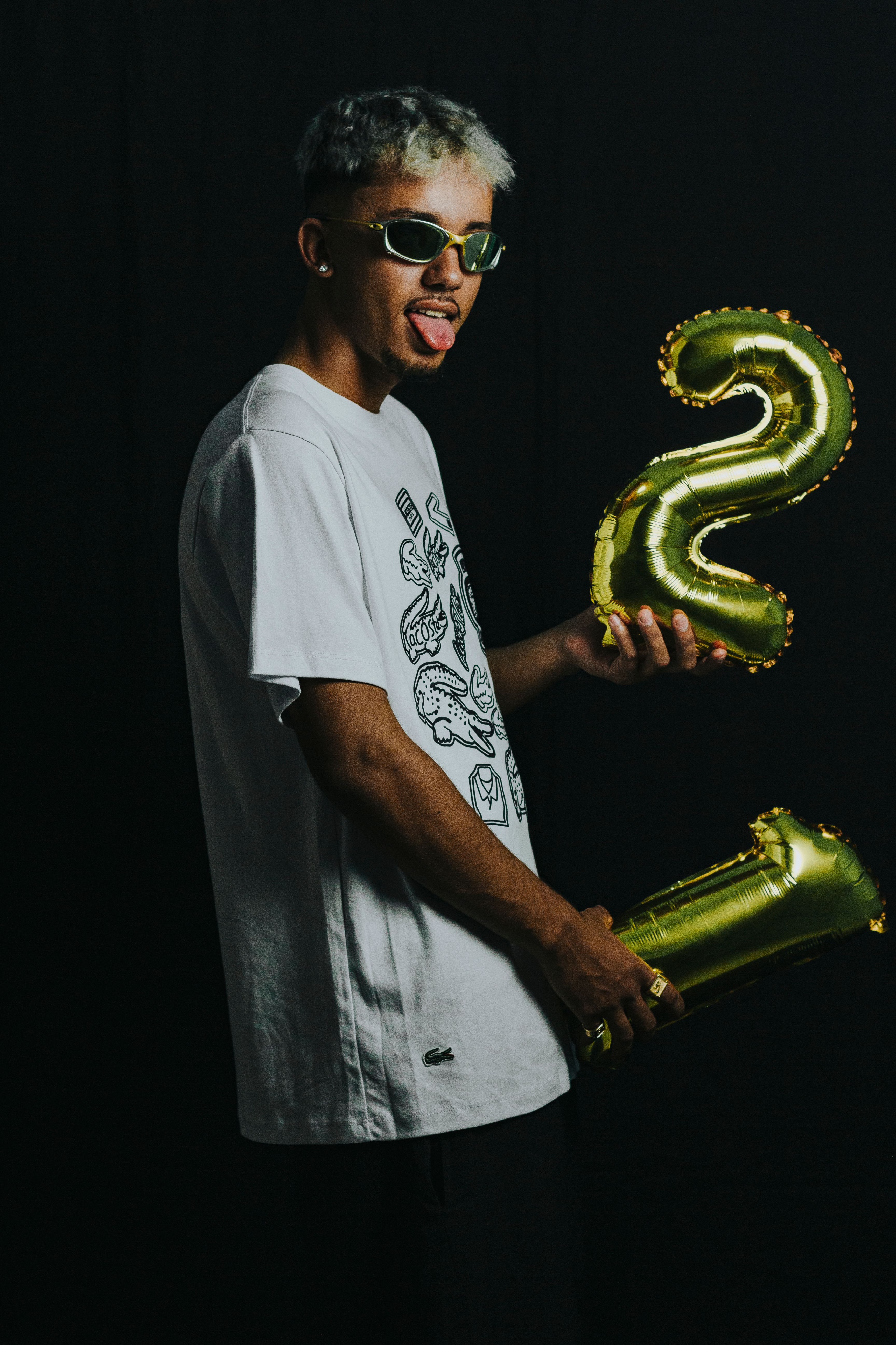 Playful man holding gold number balloons in studio with black background.