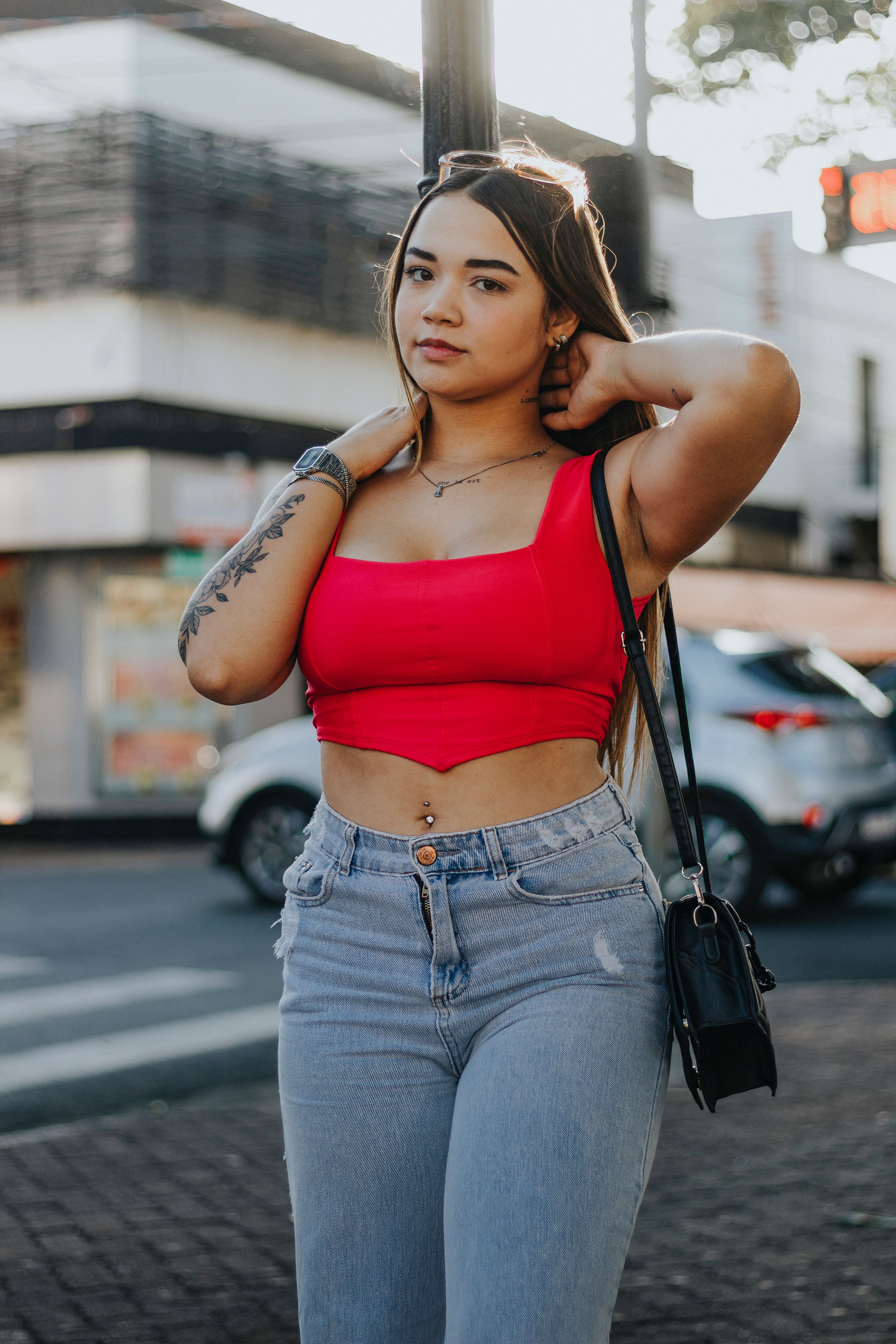 Mulher estilosa com blusa vermelha posando com confiança em uma rua da cidade.
