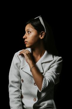 Elegant young woman posing in a white textured coat with sunglasses on head, set against a black background.