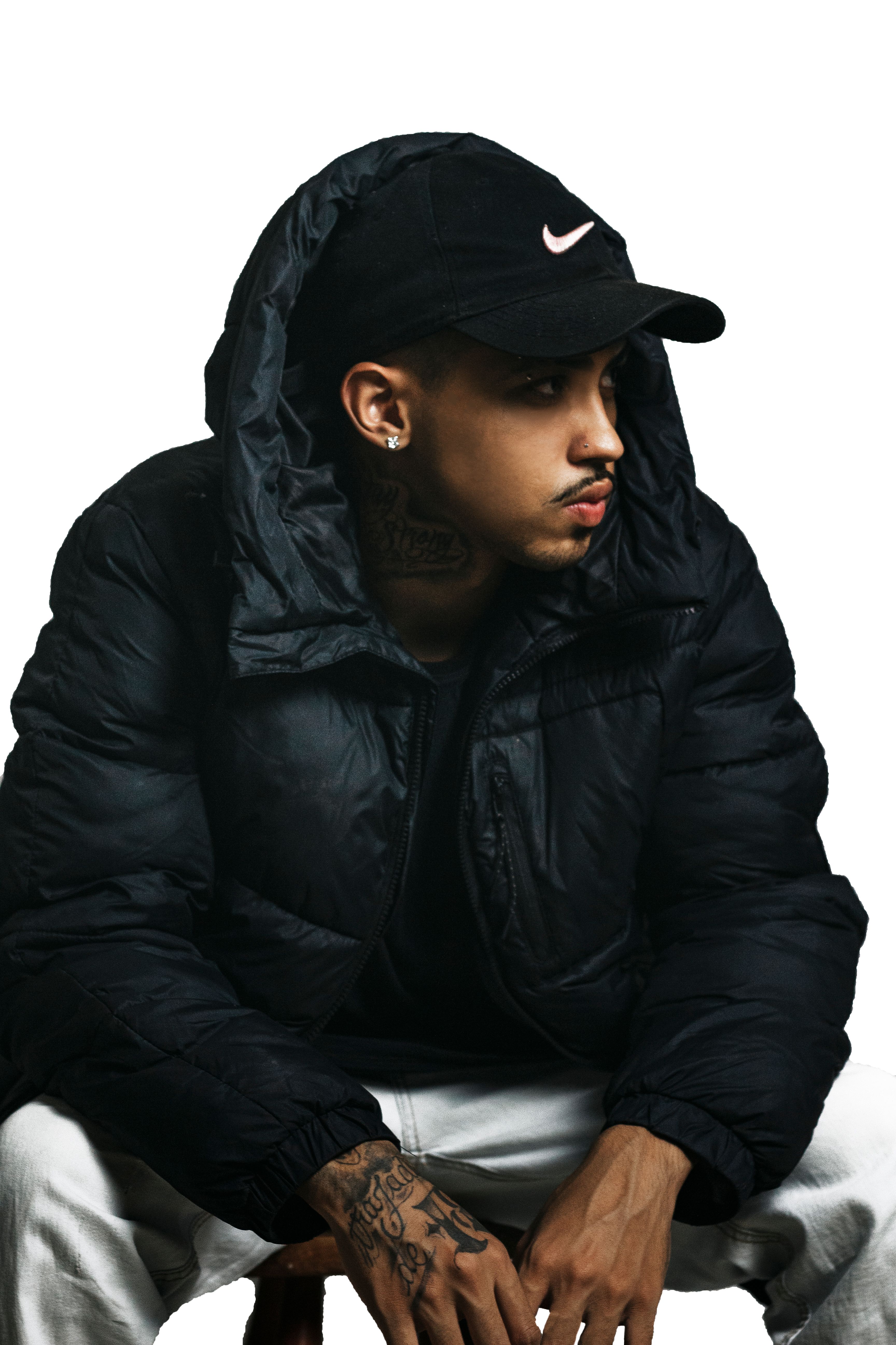 Portrait of a man in a black jacket and cap, looking sideways with a white background.