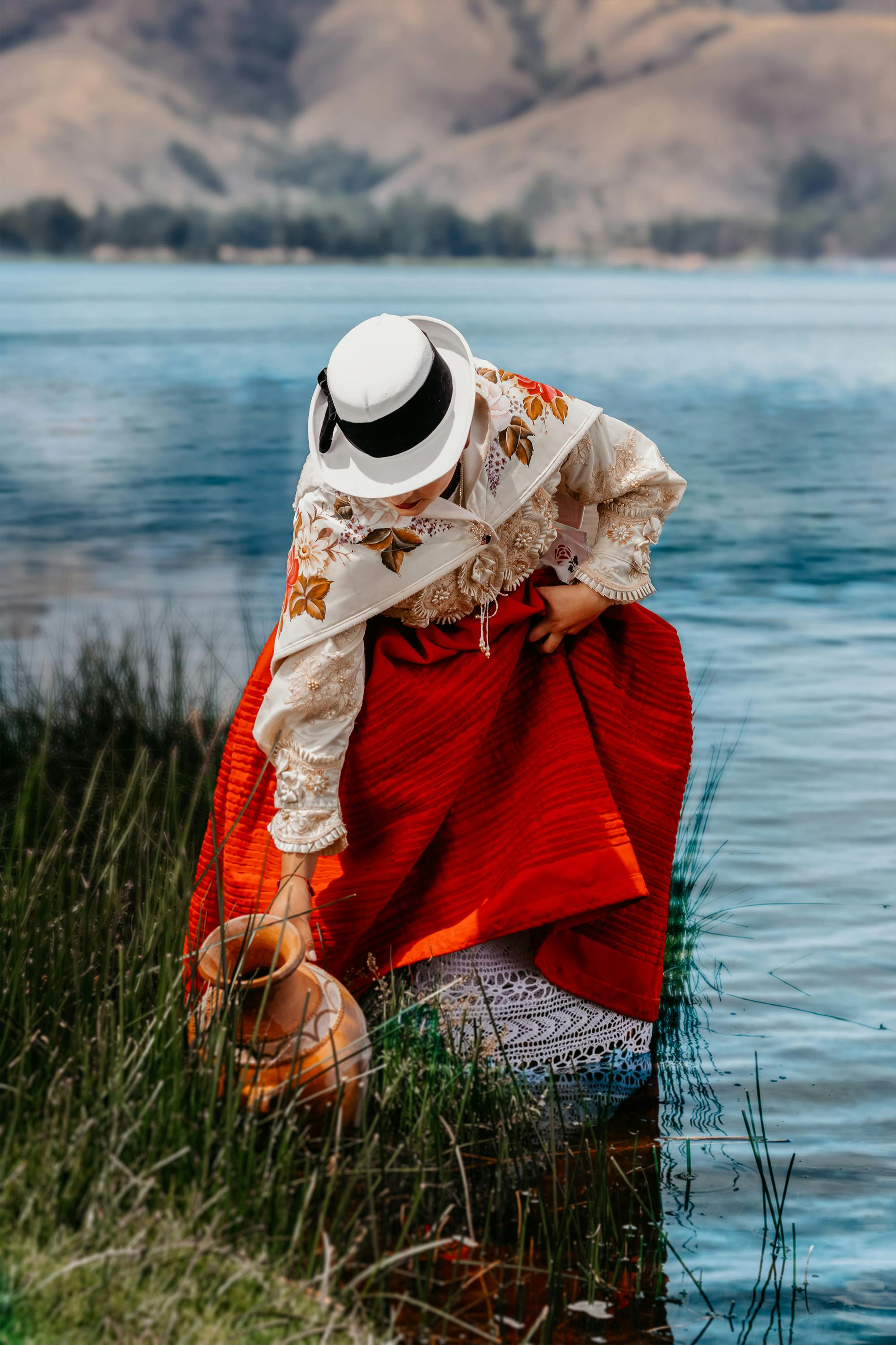 A woman in traditional Peruvian attire gathers water from a lake in Jauja, Junín, reflecting cultural heritage.