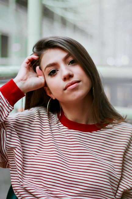 Young woman with hoop earrings in a striped sweater, posing indoors.