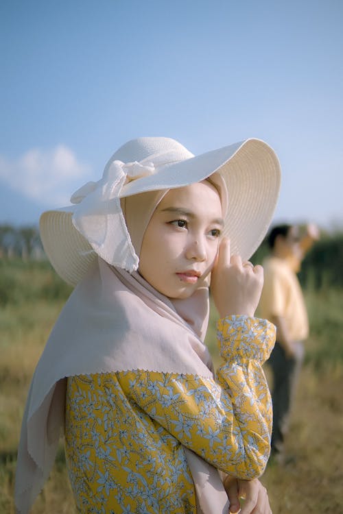 Young Elegant Woman Wearing a Dress and a Hat Posing on a Field in Summer