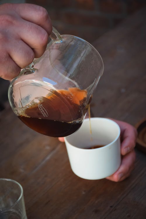 Hands Holding Pitcher and Cup and Pouring Coffee