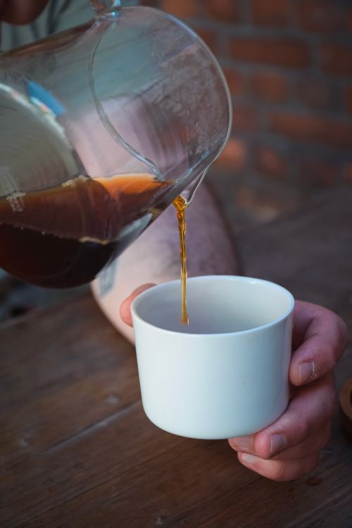 Free Close-up of coffee being poured into a white cup on a rustic wooden table. Stock Photo