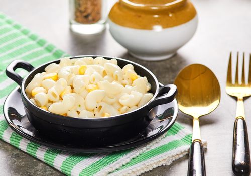 Free Delicious creamy macaroni with corn in a black bowl served with golden cutlery on a rustic table setting. Stock Photo
