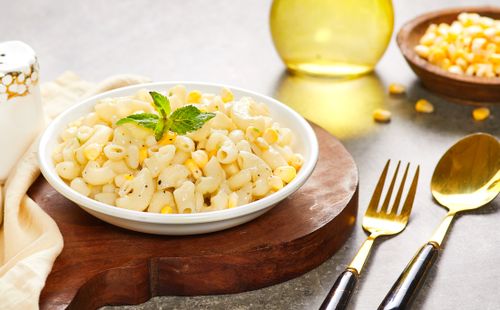 Free Delicious creamy macaroni with corn served on a rustic wooden table, perfect for lunch or dinner. Stock Photo