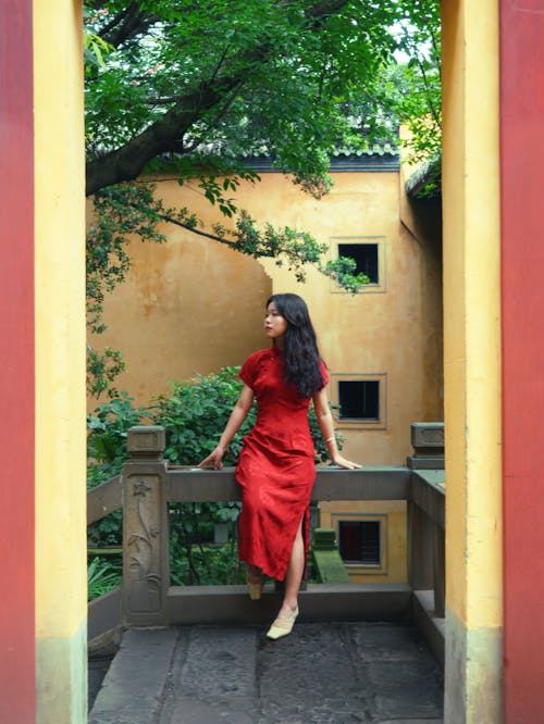 Young Brunette in a Red Dress Standing on the Porch 