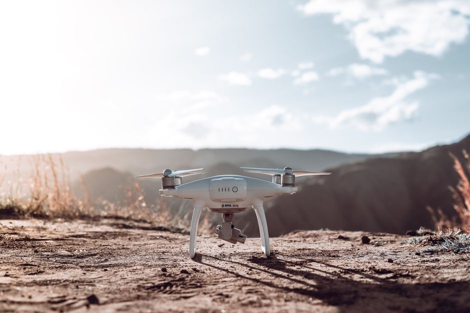 A white drone rests on a mountain terrain under a clear sky, ready for flight.