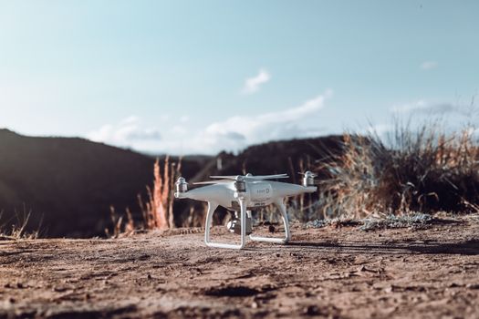 A sleek white drone rests on arid ground with scenic mountainous backdrop.