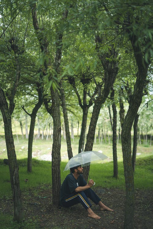 Free Barefoot Man Sitting among Trees under Umbrella Stock Photo