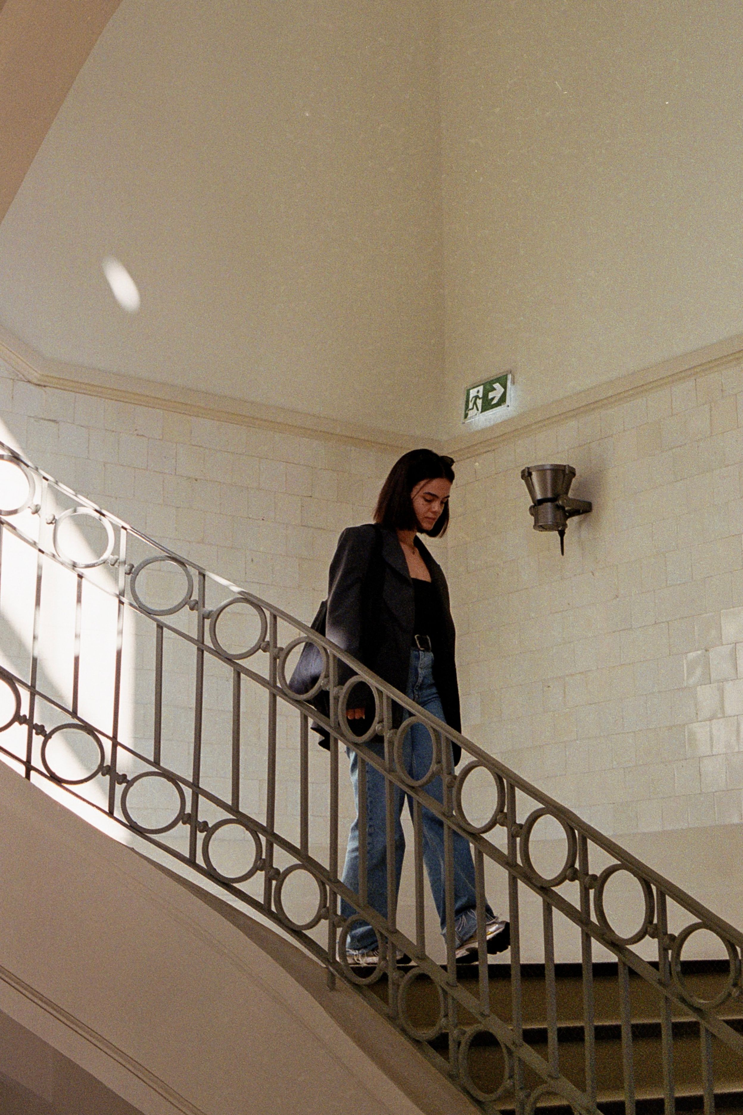 A stylish woman descends a sunlit staircase, capturing a blend of fashion and architectural elegance.