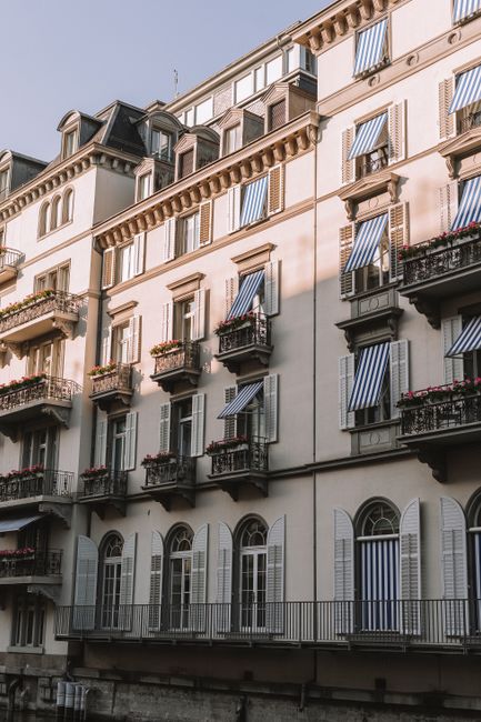 Elegant Zurich residential facade with classic architecture and striped awnings basking in sunlight.