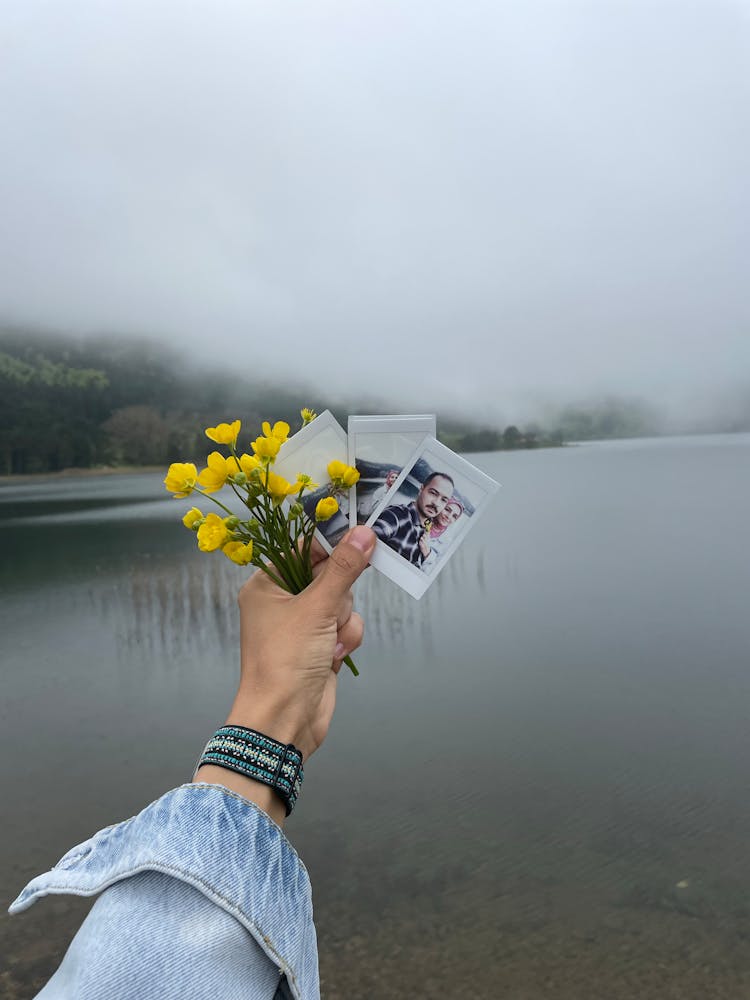 Woman Hand Holding Flowers And Pictures Over Lake