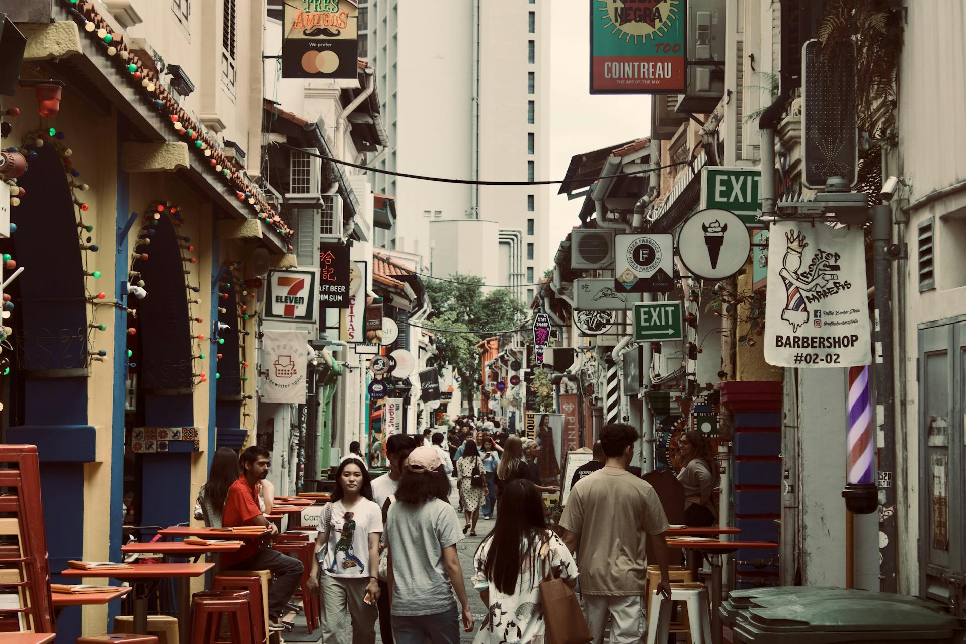 A busy alley street in Singapore filled with shops, signs, and diverse pedestrian activity.